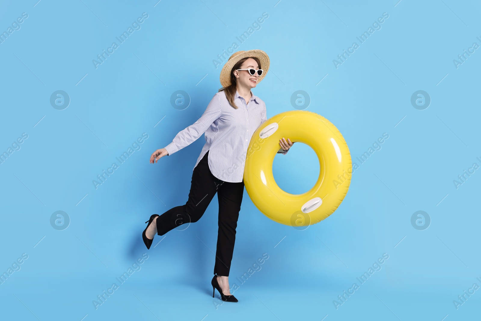 Photo of Businesswoman with inflatable ring, straw hat and sunglasses on light blue background