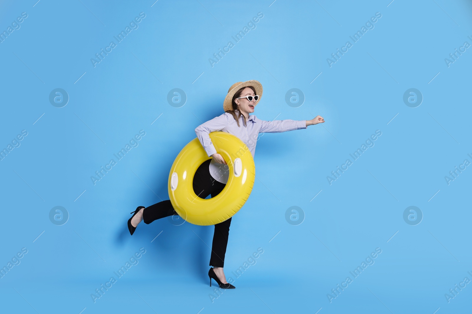 Photo of Businesswoman with inflatable ring, straw hat and sunglasses on light blue background