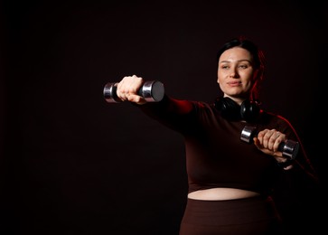 Photo of Plus size woman in gym clothes with dumbbells on black background, space for text