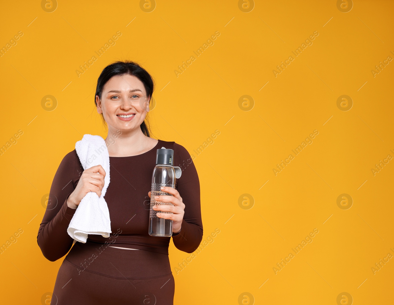 Photo of Plus size woman in gym clothes with water bottle and towel on orange background, space for text