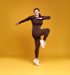 Photo of Plus size woman in gym clothes exercising on orange background