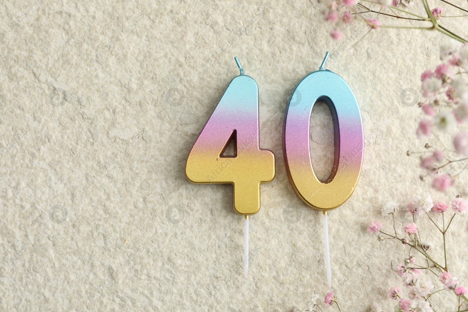 Photo of 40th birthday. Number shaped candles and flowers on light textured background, flat lay. Space for text