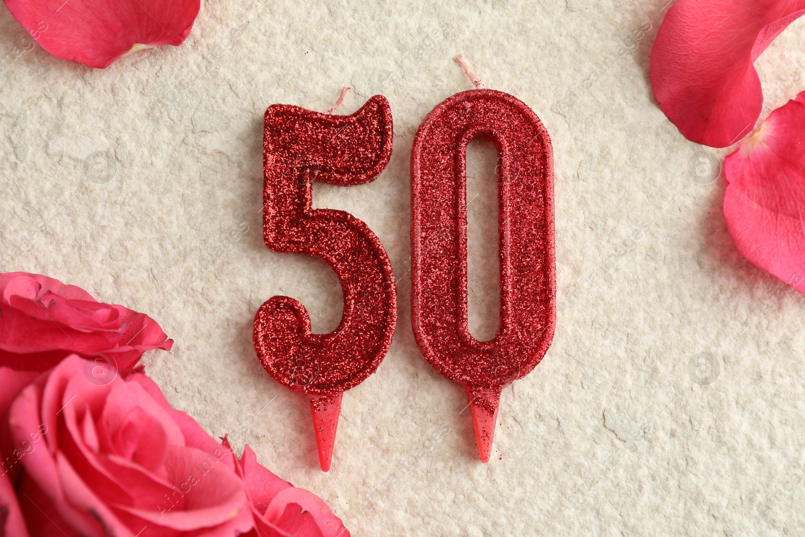 Photo of 50th birthday. Number shaped candles and roses on light textured background, flat lay