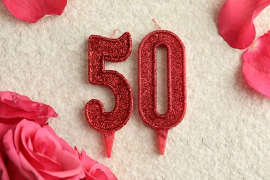 Photo of 50th birthday. Number shaped candles and roses on light textured background, flat lay