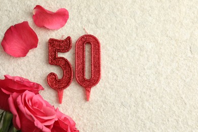 Photo of 50th birthday. Number shaped candles and roses on light textured background, flat lay. Space for text