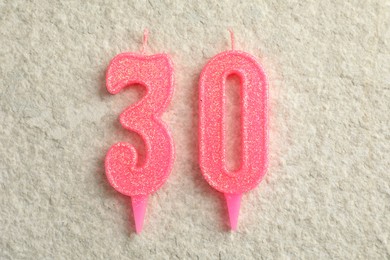 Photo of 30th birthday. Number shaped candles on light textured background, top view