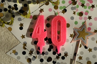 Photo of 40th birthday. Number shaped candles, party decor and confetti on light textured background, flat lay