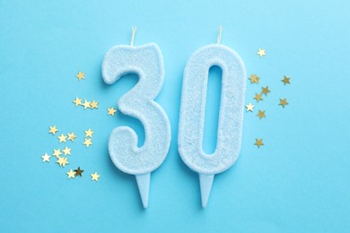 Photo of 30th birthday. Number shaped candles and confetti on light blue background, flat lay