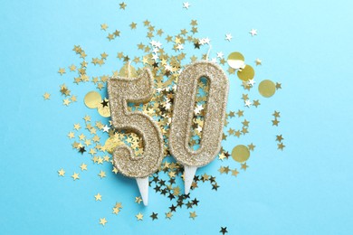 Photo of 50th birthday. Number shaped candles and confetti on light blue background, flat lay