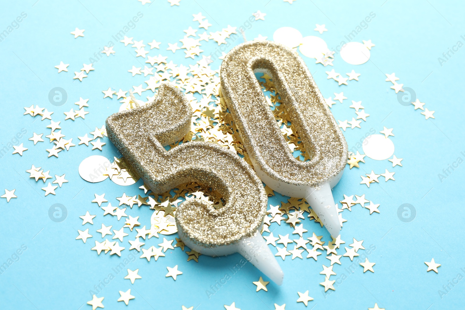 Photo of 50th birthday. Number shaped candles and confetti on light blue background, closeup