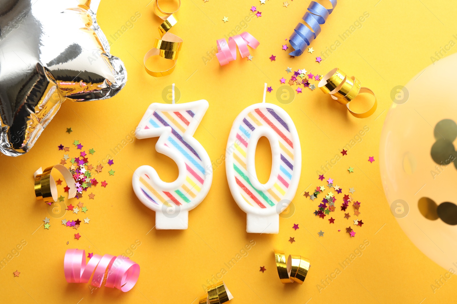 Photo of 30th birthday. Number shaped candles and party decor on orange background, flat lay