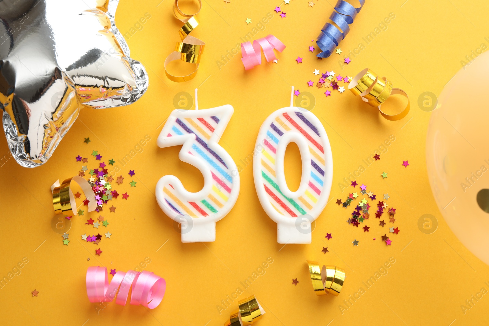 Photo of 30th birthday. Number shaped candles and party decor on orange background, flat lay