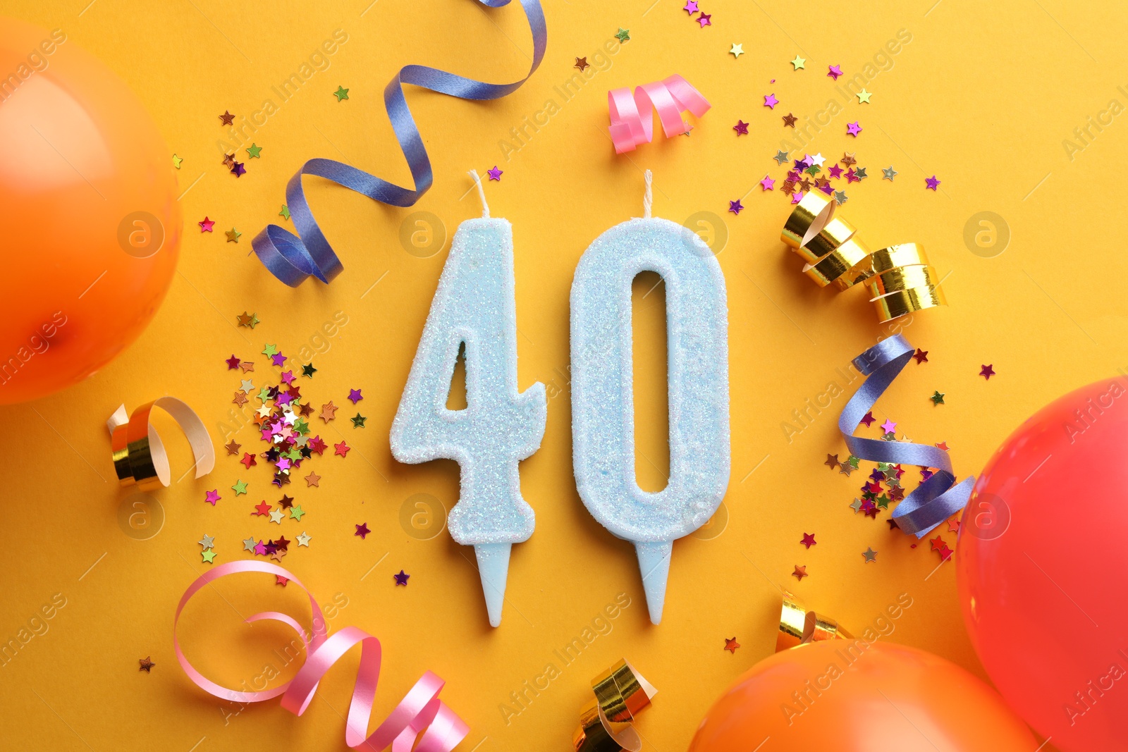 Photo of 40th birthday. Number shaped candles and party decor on orange background, flat lay