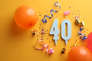 Photo of 40th birthday. Number shaped candles and party decor on orange background, flat lay