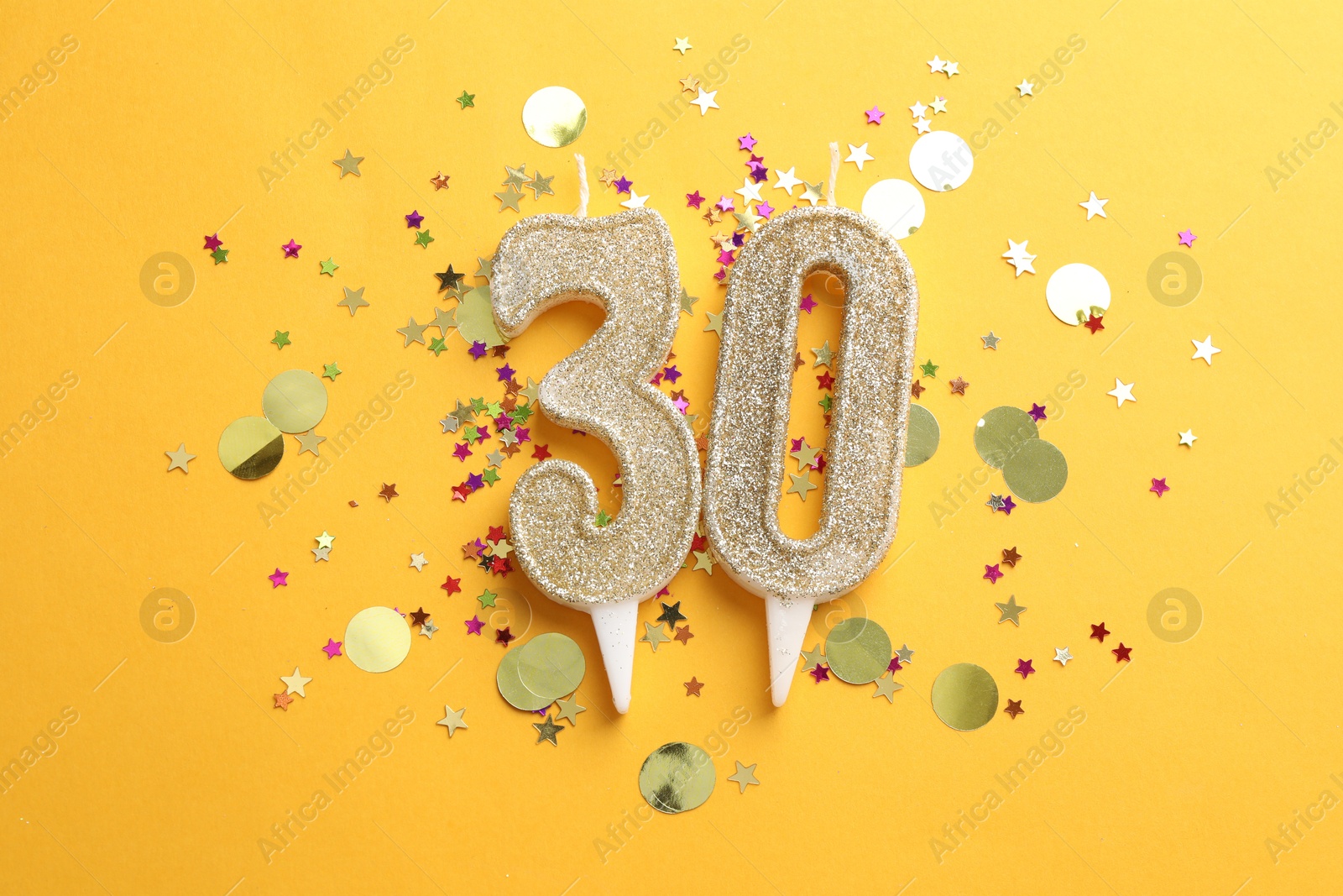 Photo of 30th birthday. Number shaped candles and confetti on orange background, flat lay