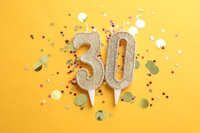 Photo of 30th birthday. Number shaped candles and confetti on orange background, flat lay