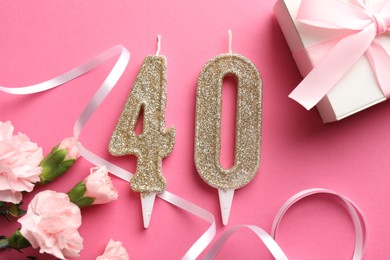 Photo of 40th birthday. Number shaped candles, gift and flowers on pink background, flat lay