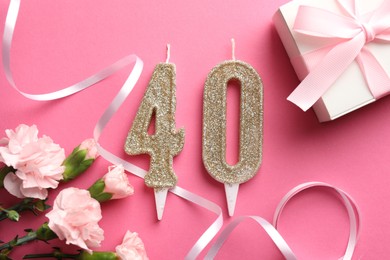 Photo of 40th birthday. Number shaped candles, gift and flowers on pink background, flat lay