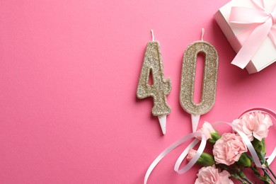 Photo of 40th birthday. Number shaped candles, gift and flowers on pink background, flat lay. Space for text