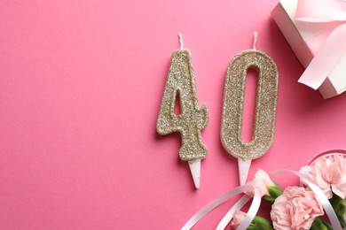 Photo of 40th birthday. Number shaped candles, gift and flowers on pink background, flat lay. Space for text