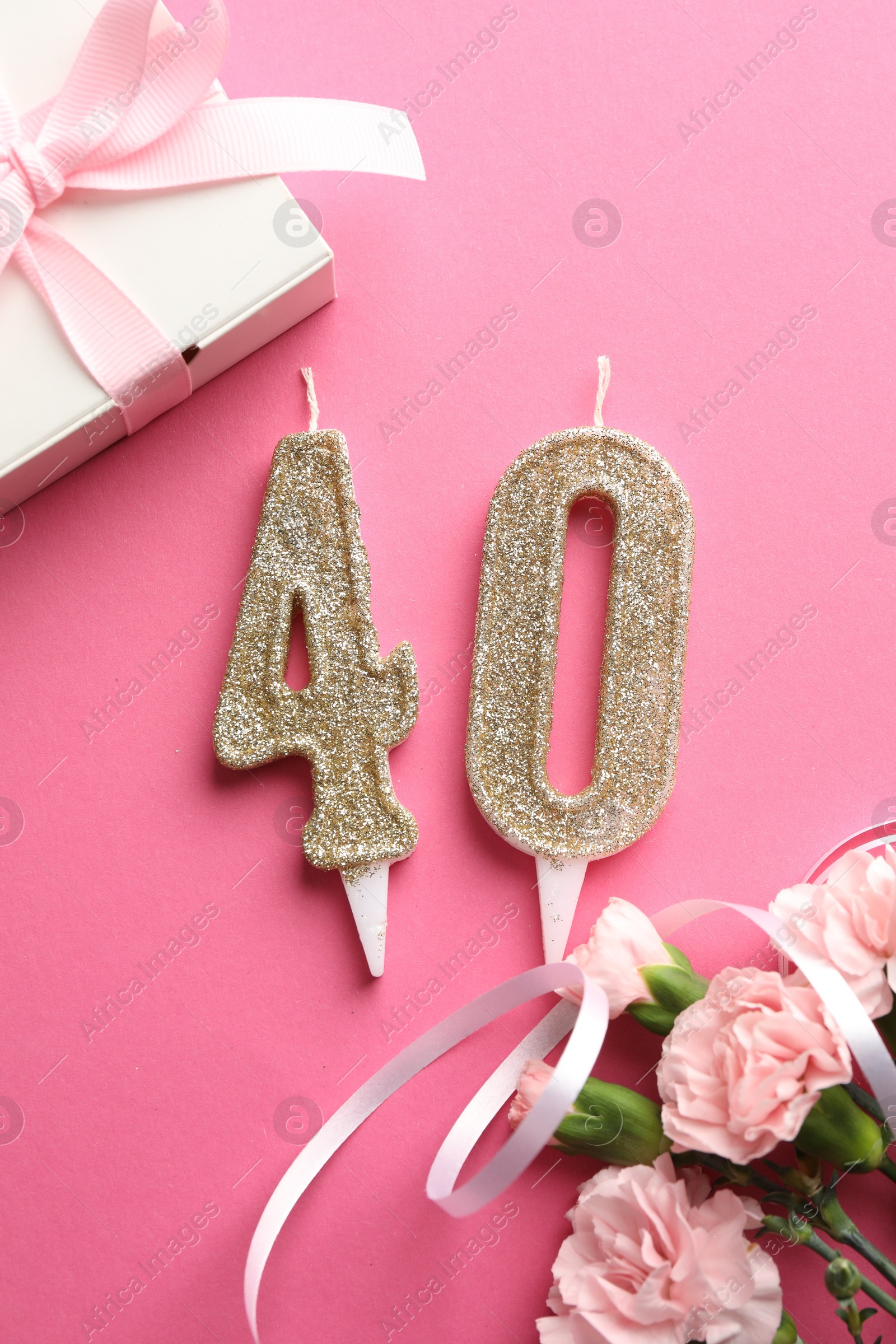 Photo of 40th birthday. Number shaped candles, gift and flowers on pink background, flat lay