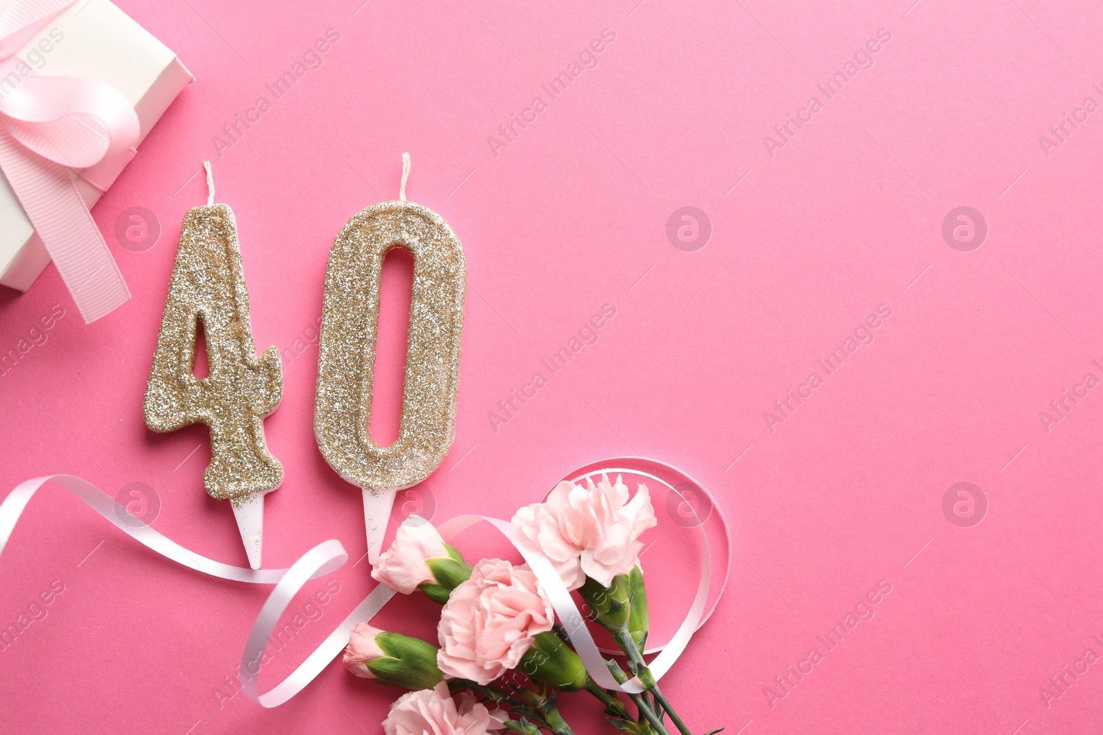 Photo of 40th birthday. Number shaped candles, gift and flowers on pink background, flat lay. Space for text