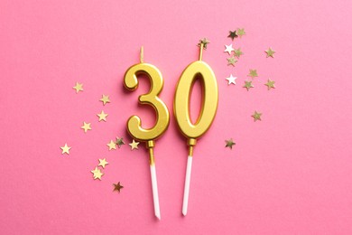 Photo of 30th birthday. Number shaped candles and confetti on pink background, flat lay