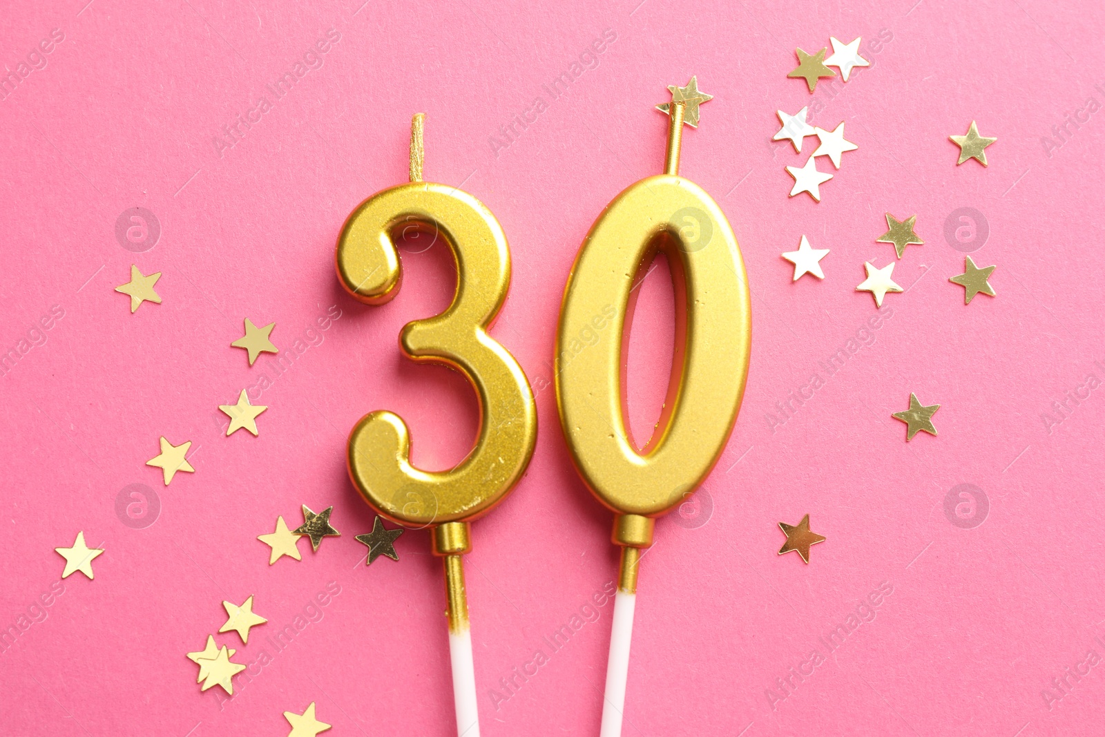 Photo of 30th birthday. Number shaped candles and confetti on pink background, flat lay