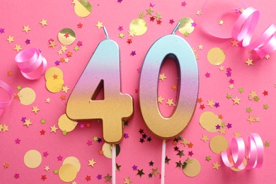 Photo of 40th birthday. Number shaped candles and confetti on pink background, flat lay