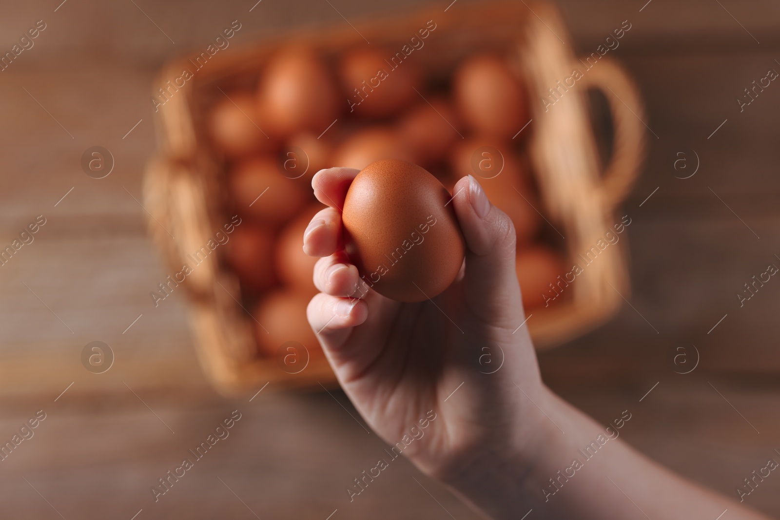 Photo of Woman holding raw egg above wooden table, top view