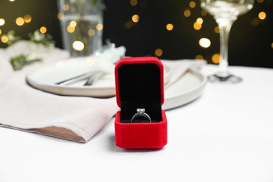 Engagement ring in box on white tablecloth, closeup. Romantic dinner