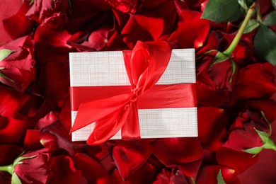 Photo of Beautiful gift box among rose flowers and petals, top view. Romantic present