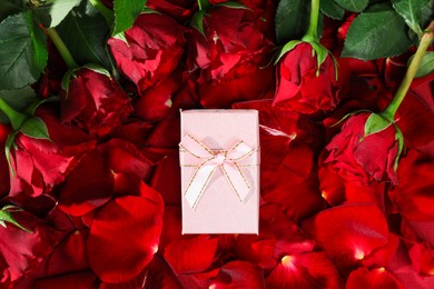 Photo of Beautiful gift box among rose flowers and petals, top view. Romantic present