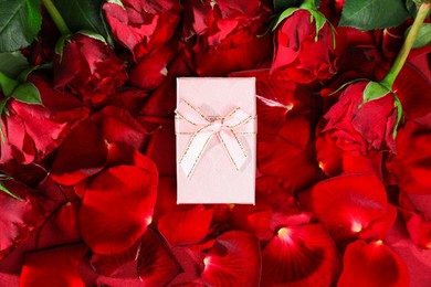 Beautiful gift box among rose flowers and petals, top view. Romantic present