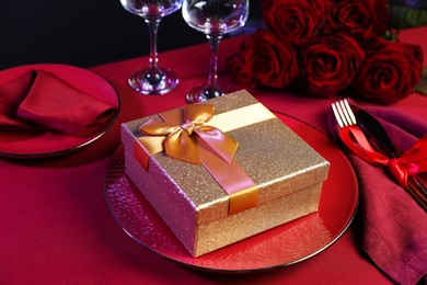 Gift box, tableware and roses on red table, closeup. Table setting for romantic dinner