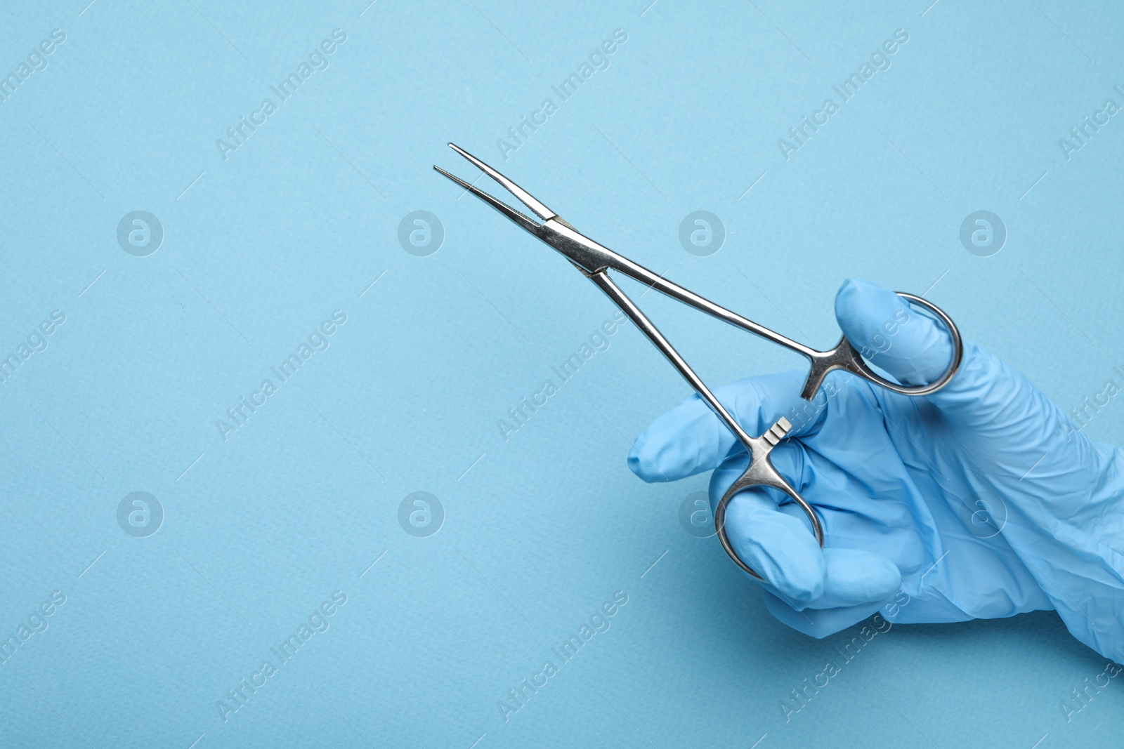 Photo of Doctor with surgical forceps on light blue background, closeup. Space for text