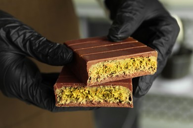 Photo of Woman holding pieces of tasty Dubai chocolate with pistachios and knafeh indoors, closeup