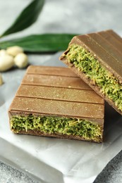 Photo of Pieces of tasty Dubai chocolate with pistachios and knafeh on grey textured table, closeup