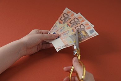 Photo of Woman cutting euro banknotes on brown background, closeup