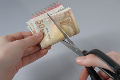 Photo of Woman cutting euro banknotes on gray background, closeup