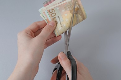 Photo of Woman cutting euro banknotes on gray background, closeup