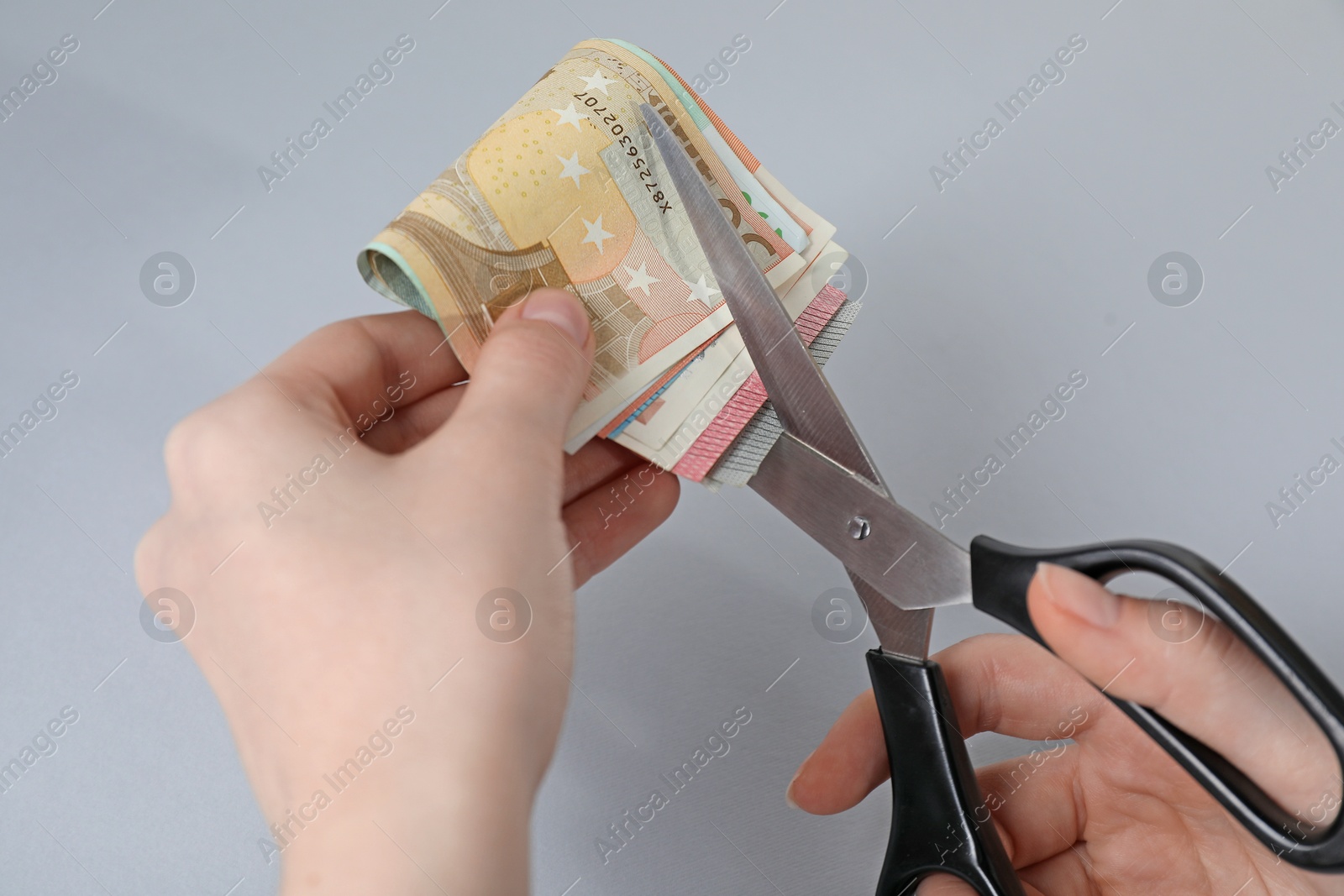 Photo of Woman cutting euro banknotes on gray background, closeup