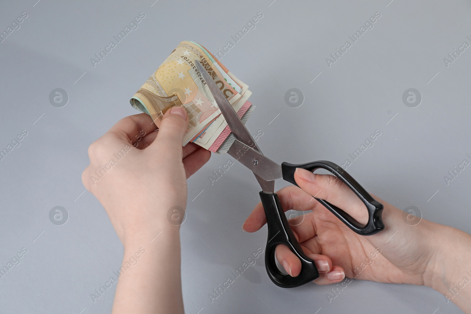 Photo of Woman cutting euro banknotes on gray background, closeup