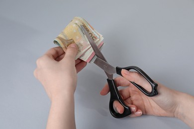 Photo of Woman cutting euro banknotes on gray background, closeup