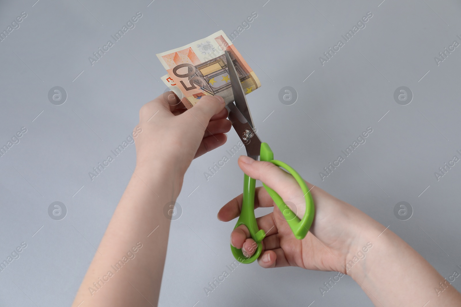 Photo of Woman cutting euro banknote on gray background, closeup