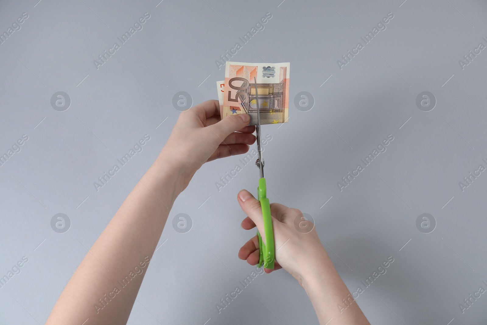 Photo of Woman cutting euro banknote on gray background, top view