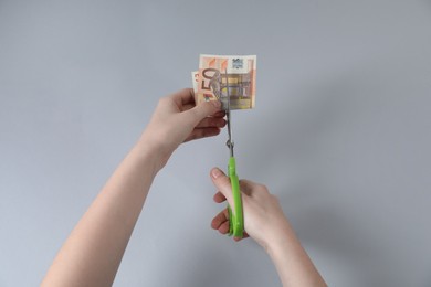 Photo of Woman cutting euro banknote on gray background, top view