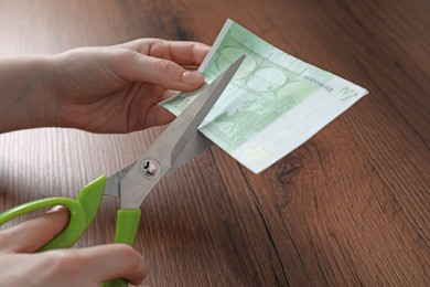 Photo of Woman cutting euro banknote at wooden table, closeup