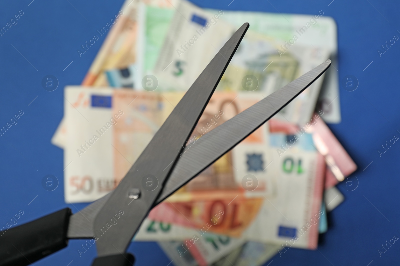 Photo of Scissors and euro banknote on blue background, selective focus