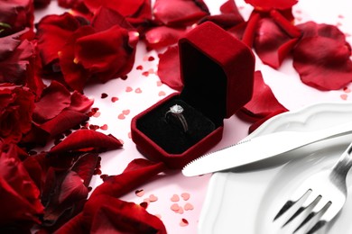 Photo of Beautiful setting for romantic dinner, engagement ring and rose petals on light pink table, closeup